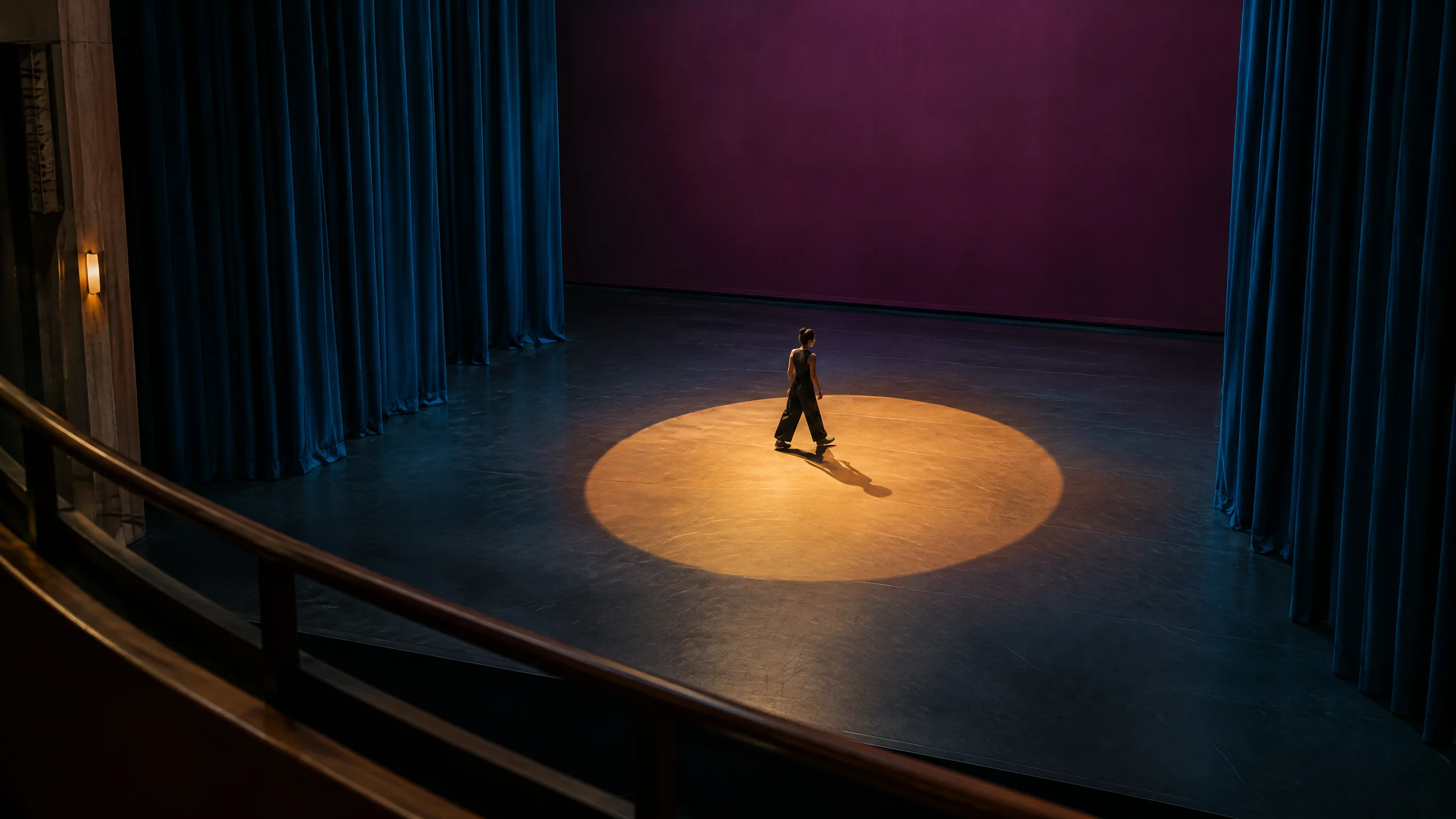 Figure crossing an empty amber-lit rehearsal stage